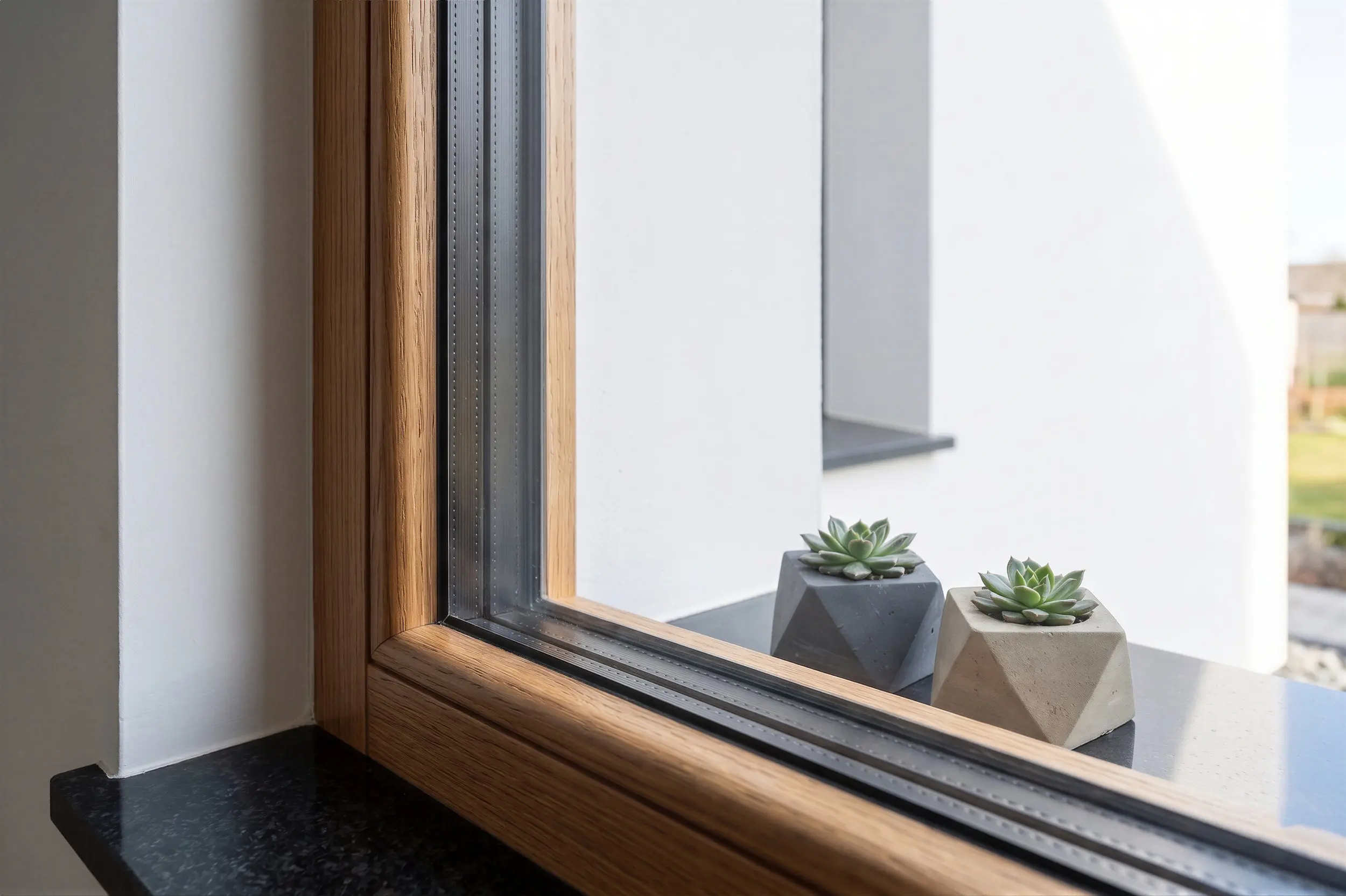 Detailaufnahme eines Holzfensters nach einem Glastausch. Zu sehen ist ein modernes 3-fach-Isolierglas mit schwarzem Randverbund (warme Kante) in einem hochwertigen Holzrahmen auf einer dunklen Fensterbank.